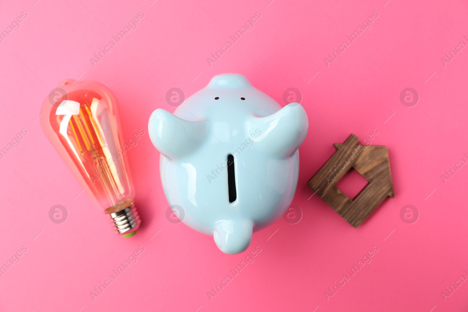 Photo of Piggy bank, light bulb and wooden house model on pink background, flat lay. Energy saving concept