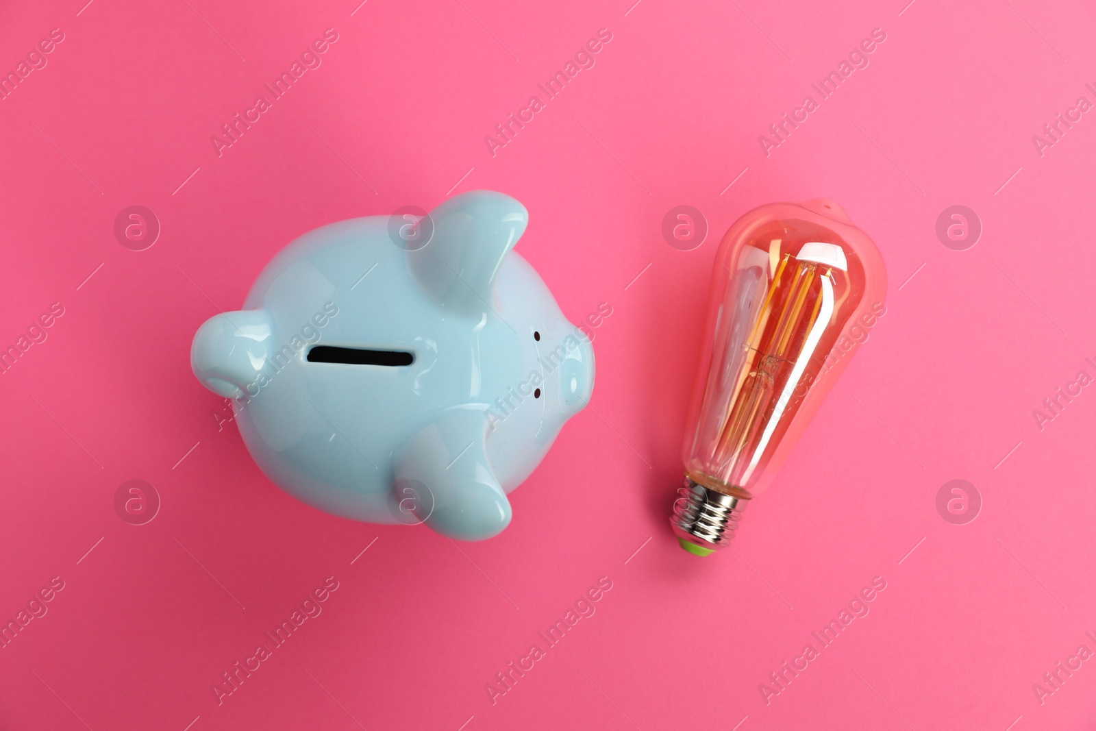 Photo of Piggy bank and light bulb on pink background, flat lay. Energy saving concept