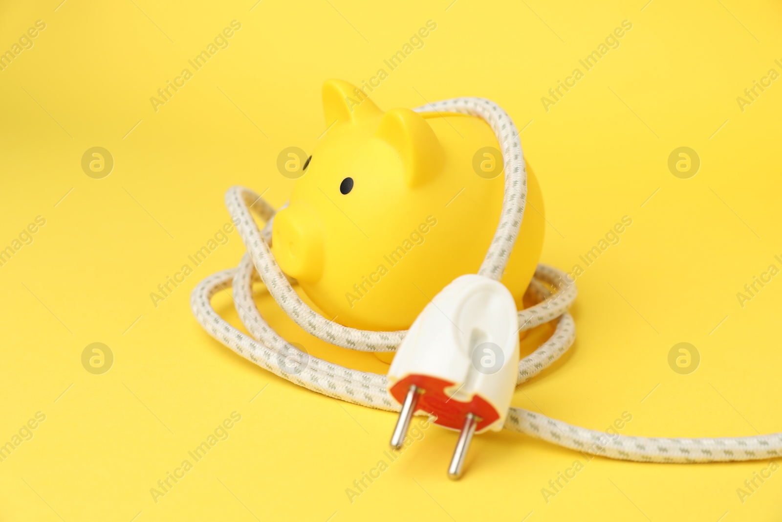 Photo of Piggy bank with plug on yellow background, closeup. Energy saving concept