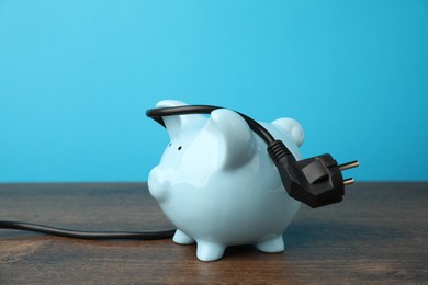 Photo of Piggy bank and plug on wooden table. Energy saving concept