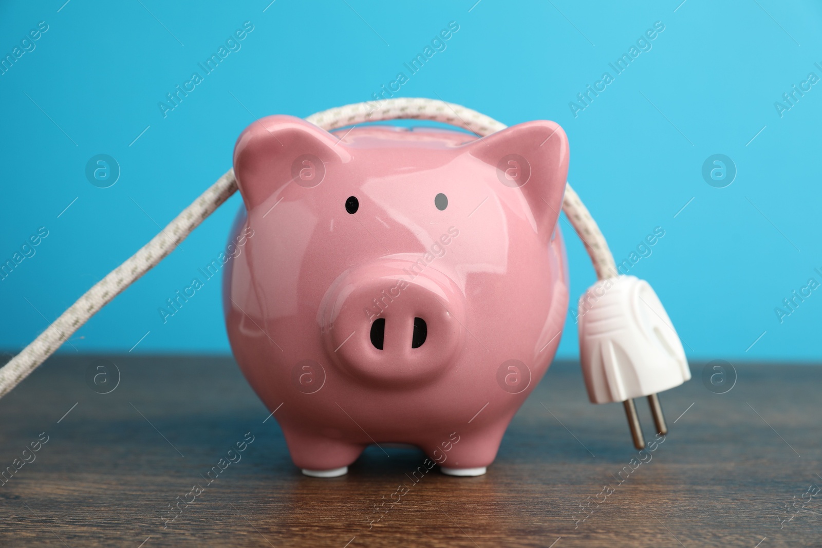 Photo of Piggy bank and plug on wooden table, closeup. Energy saving concept