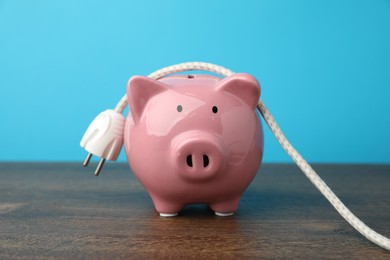 Photo of Piggy bank and plug on wooden table, closeup. Energy saving concept