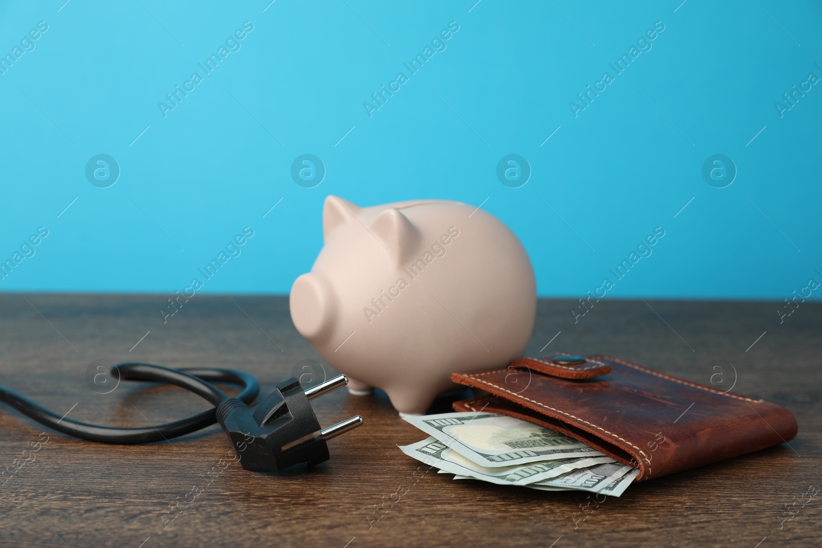 Photo of Piggy bank, plug and dollar banknotes on wooden table, closeup. Energy saving concept