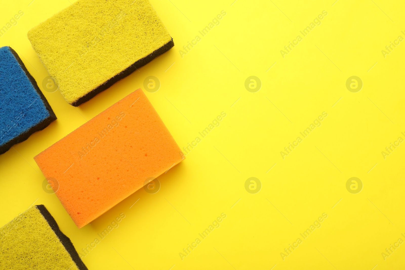 Photo of Many color sponges on yellow background, flat lay. Space for text