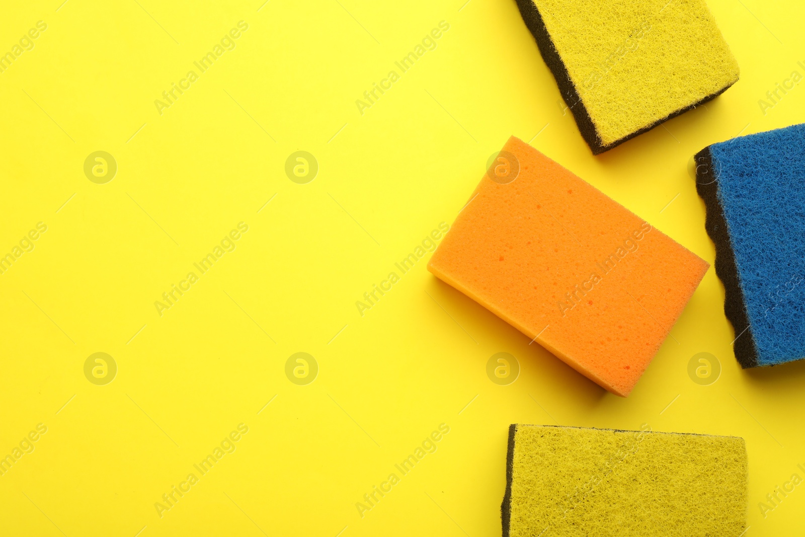 Photo of Many color sponges on yellow background, flat lay. Space for text