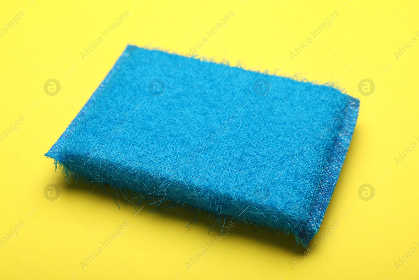 Photo of One blue sponge on yellow background, closeup