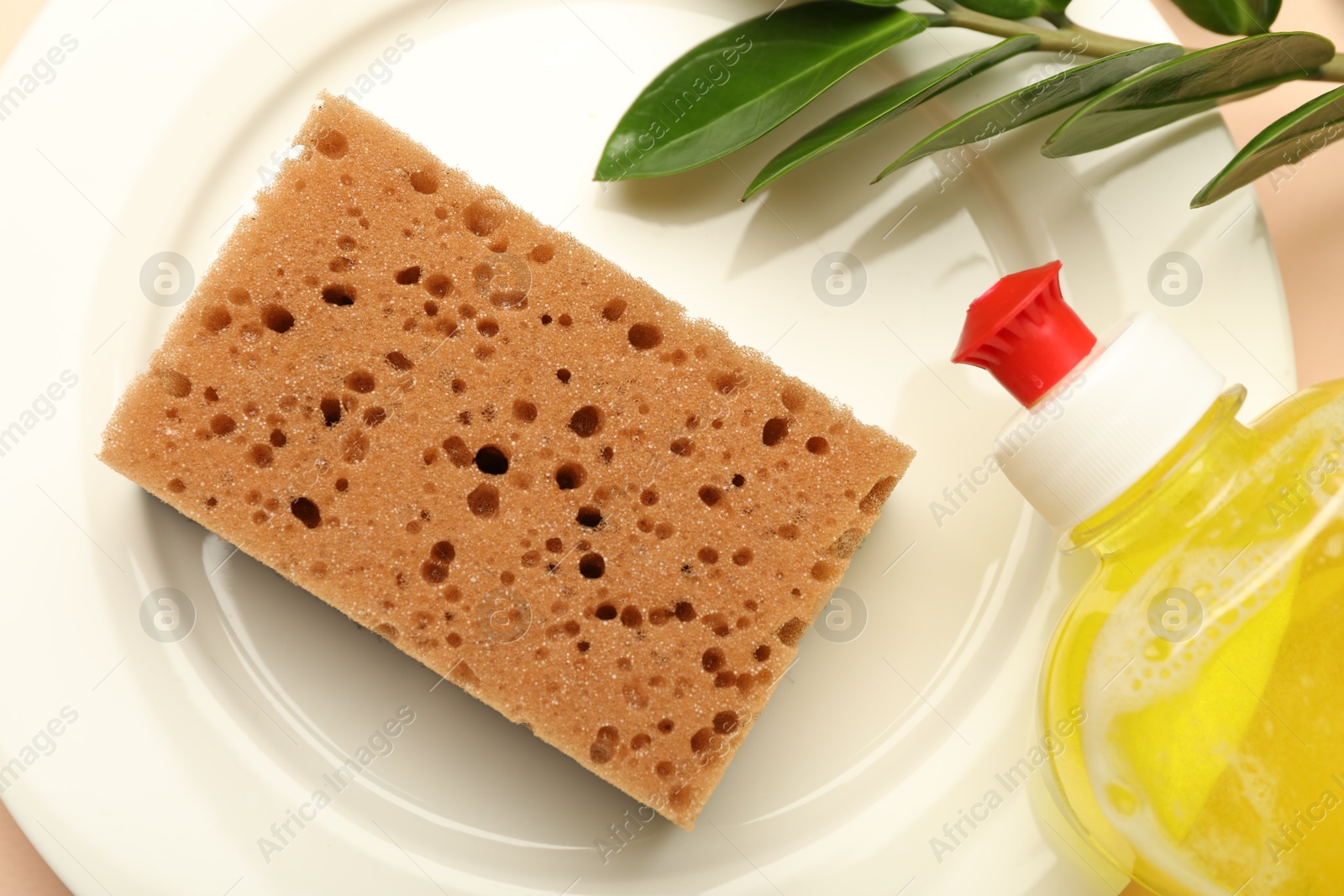 Photo of Sponge, detergent and plate on beige background, flat lay