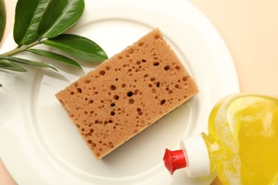 Photo of Sponge, detergent and plate on beige background, flat lay