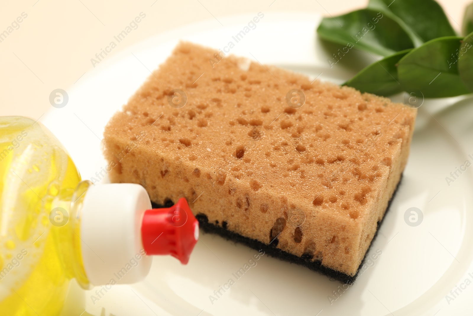 Photo of Sponge, detergent and plate on beige background, closeup