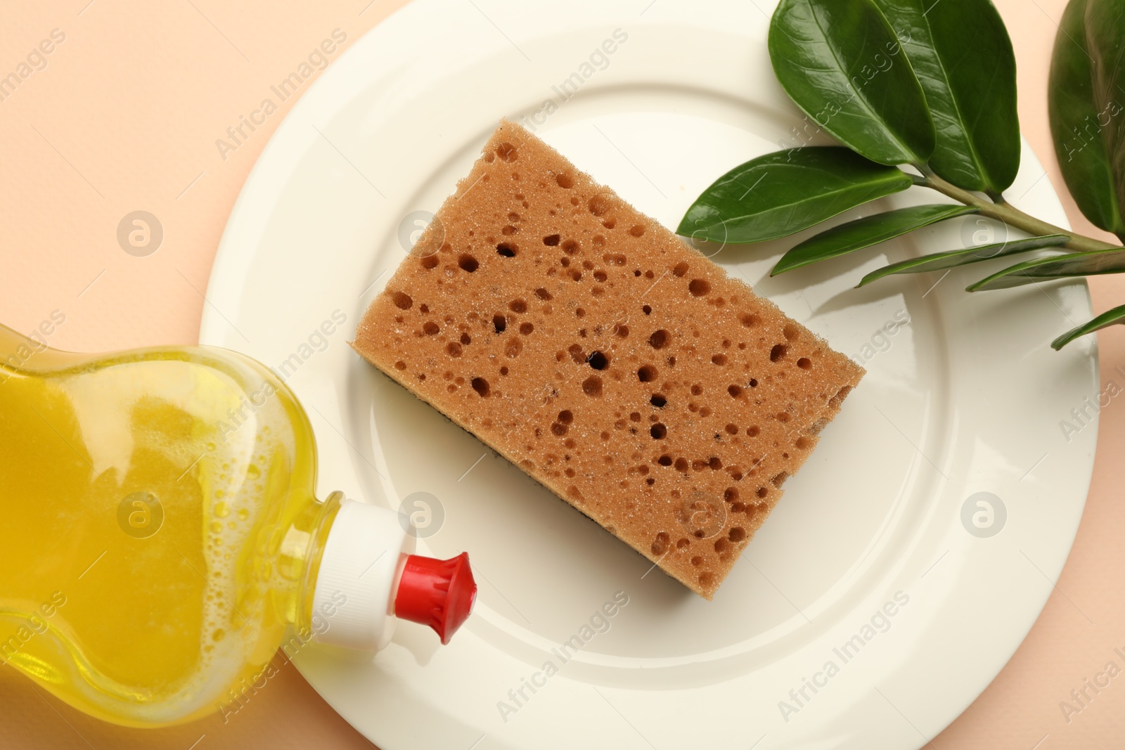 Photo of Sponge, detergent and plate on beige background, flat lay