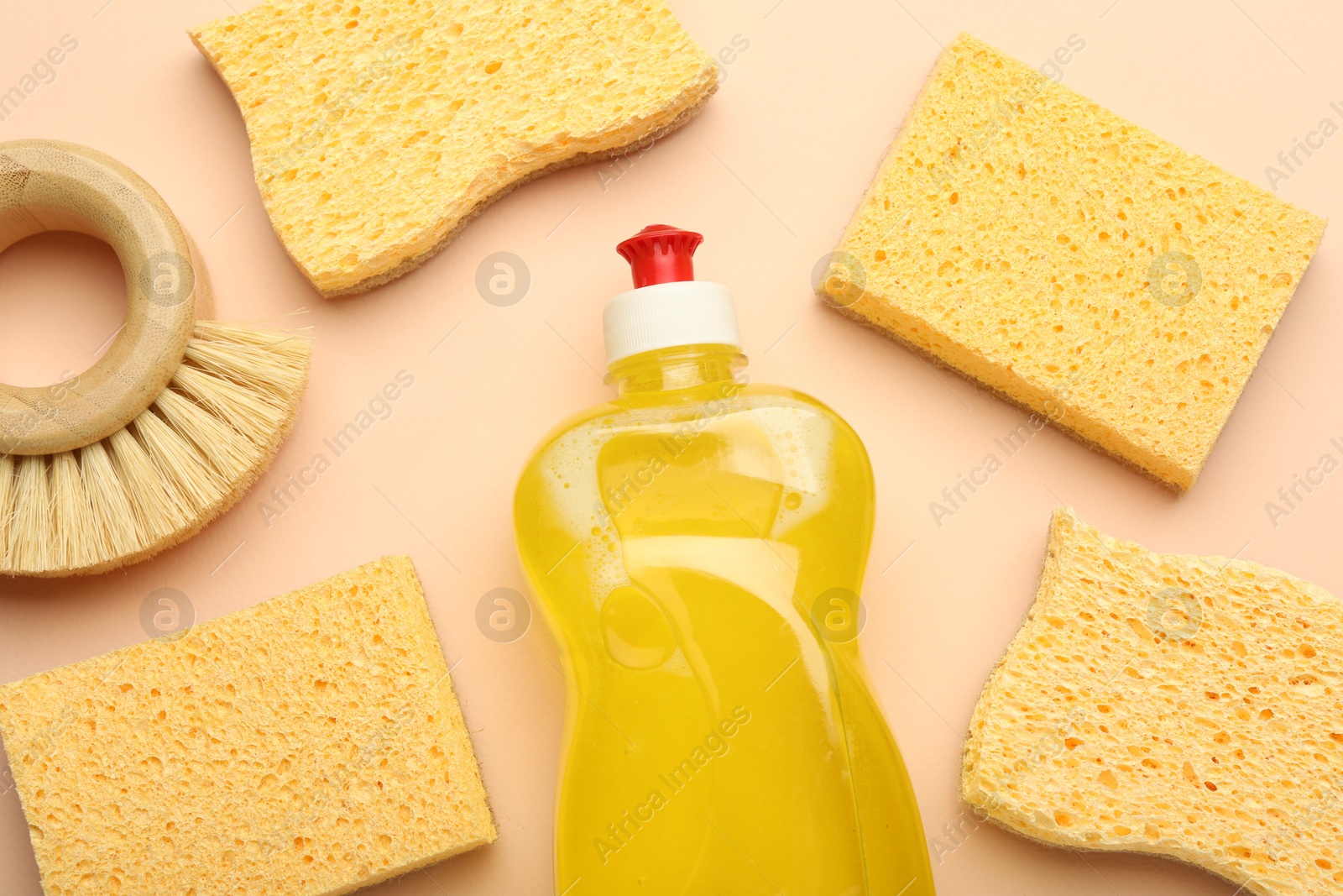 Photo of Many sponges, brush and bottle of detergent on beige background, flat lay