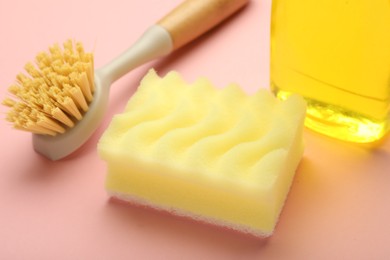 Photo of Sponge, brush and detergent on pink background, closeup