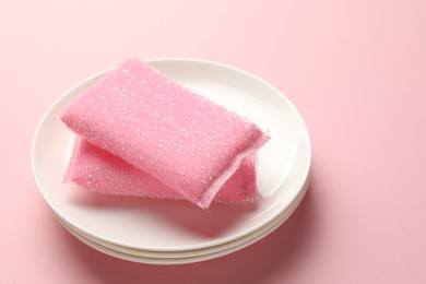 Photo of Sponges and stack of plates on pink background, closeup