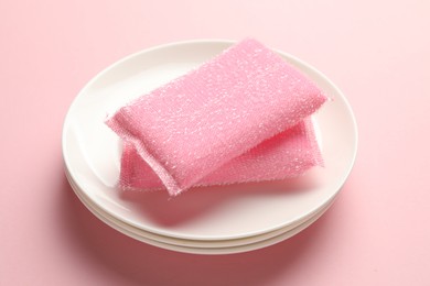 Photo of Sponges and stack of plates on pink background, closeup