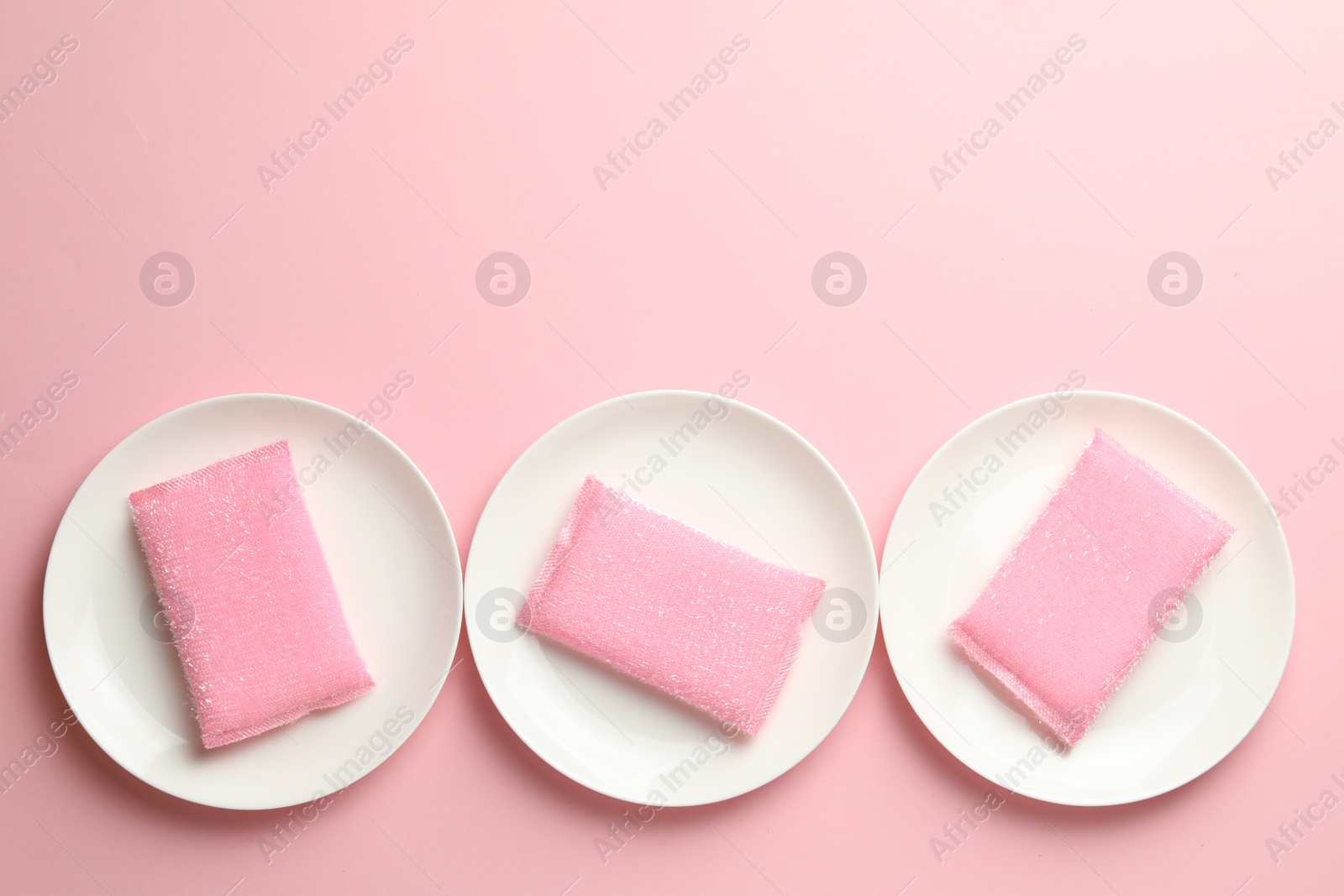 Photo of Sponges and plates on pink background, flat lay. Space for text