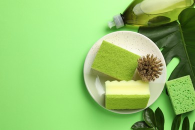 Photo of Flat lay composition with sponges, brush and detergent on green background. Space for text