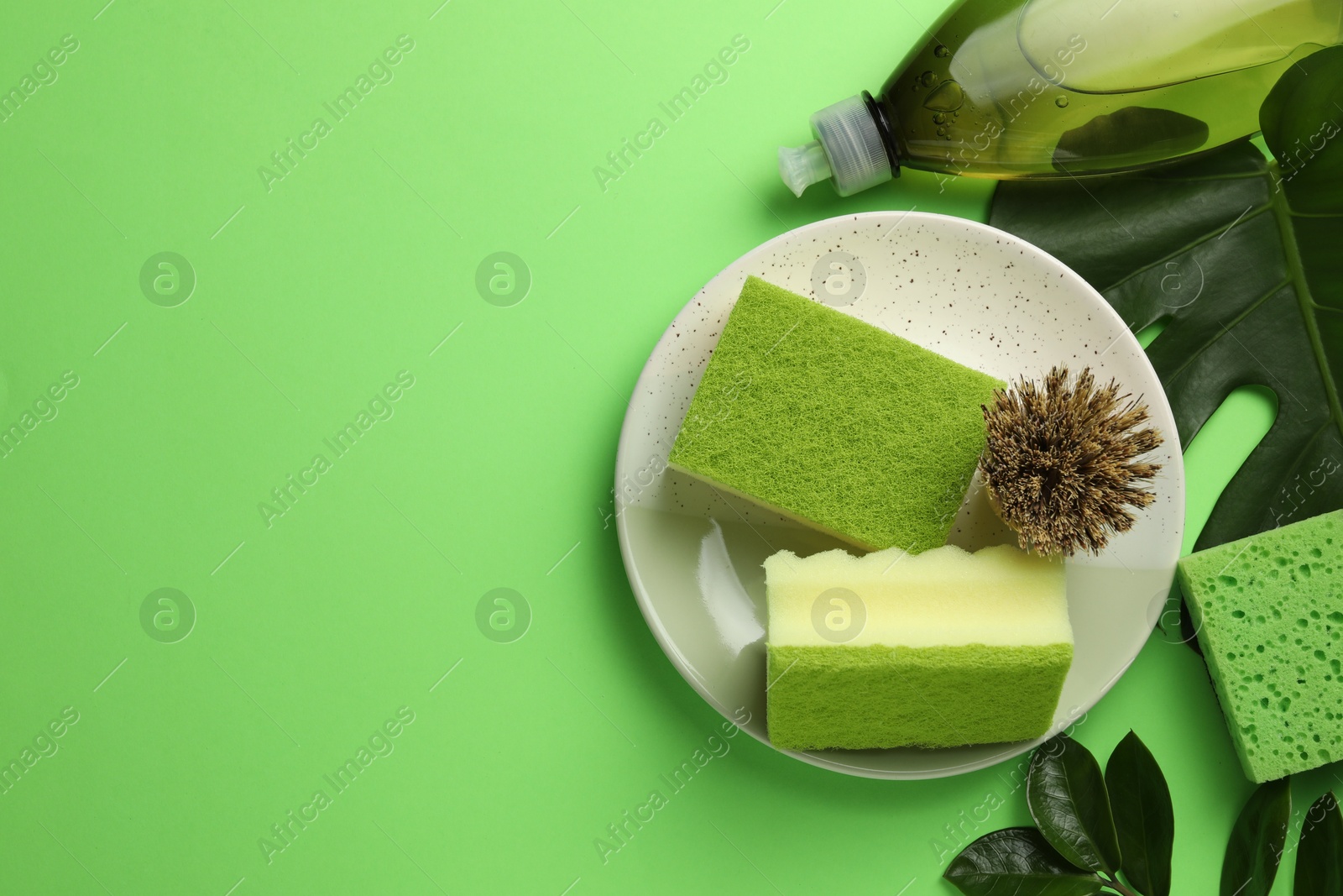 Photo of Flat lay composition with sponges, brush and detergent on green background. Space for text