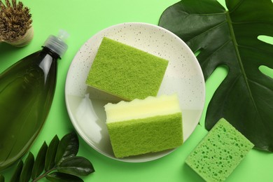 Flat lay composition with sponges, brush and detergent on green background