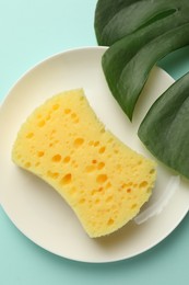 Photo of One sponge, plate and monstera leaf on light blue background, top view