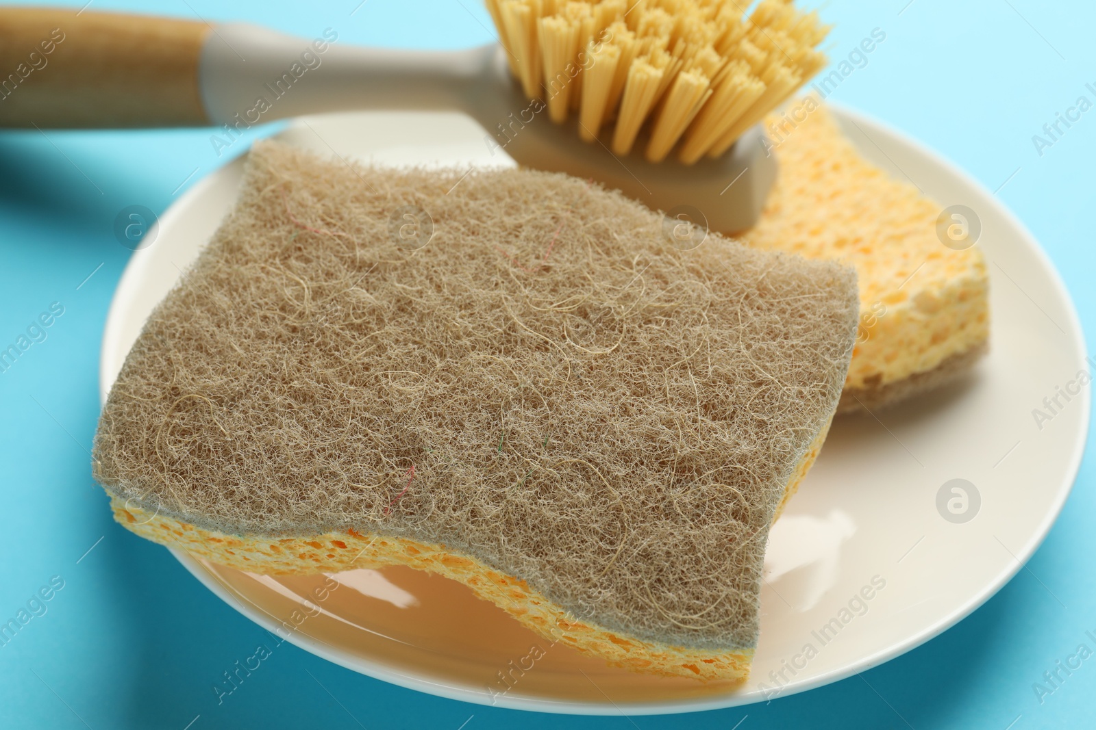 Photo of Sponges, plate and brush on light blue background, closeup