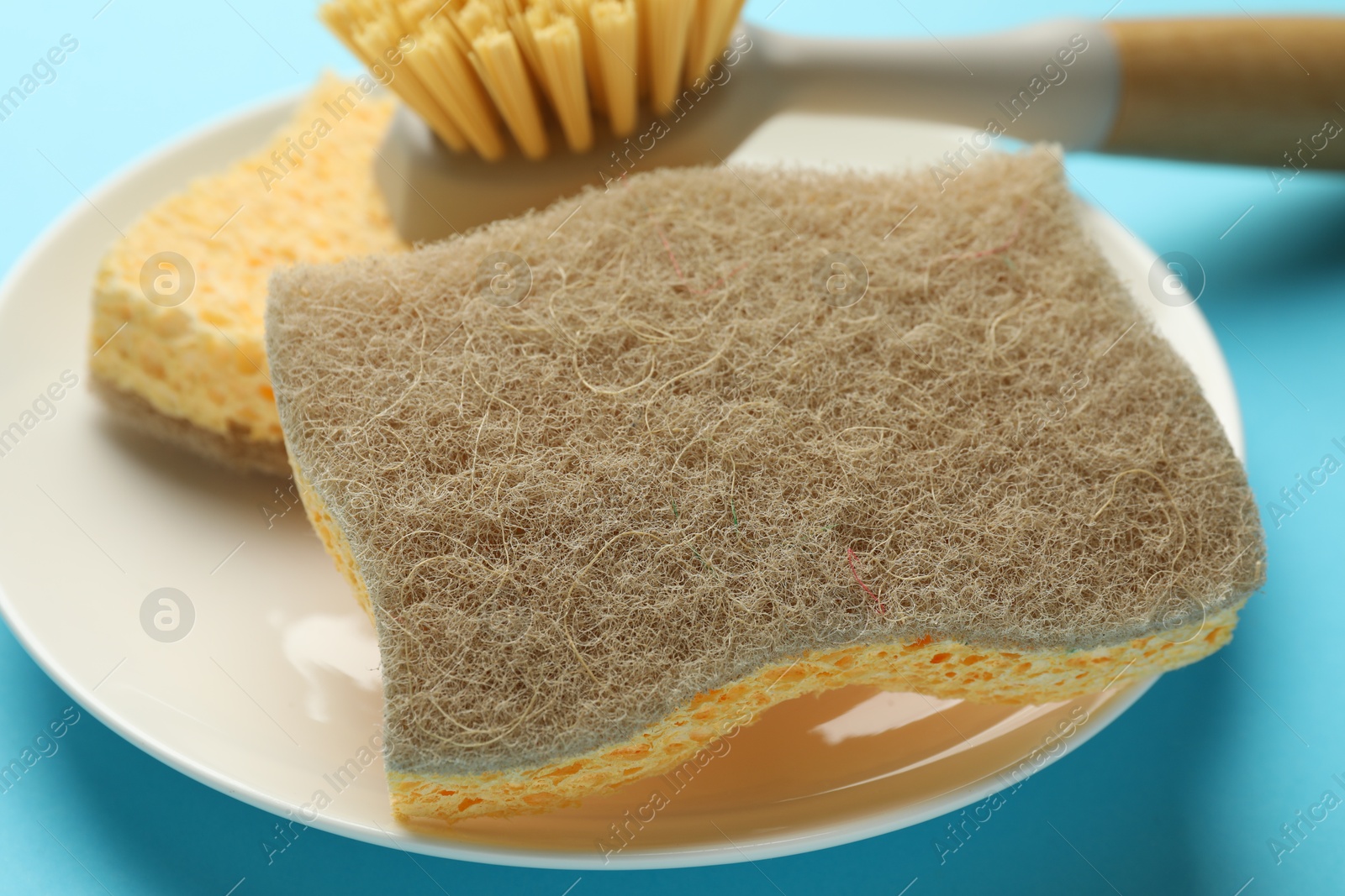 Photo of Sponges, plate and brush on light blue background, closeup