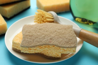 Photo of Sponges, plate and brush on light blue background, closeup