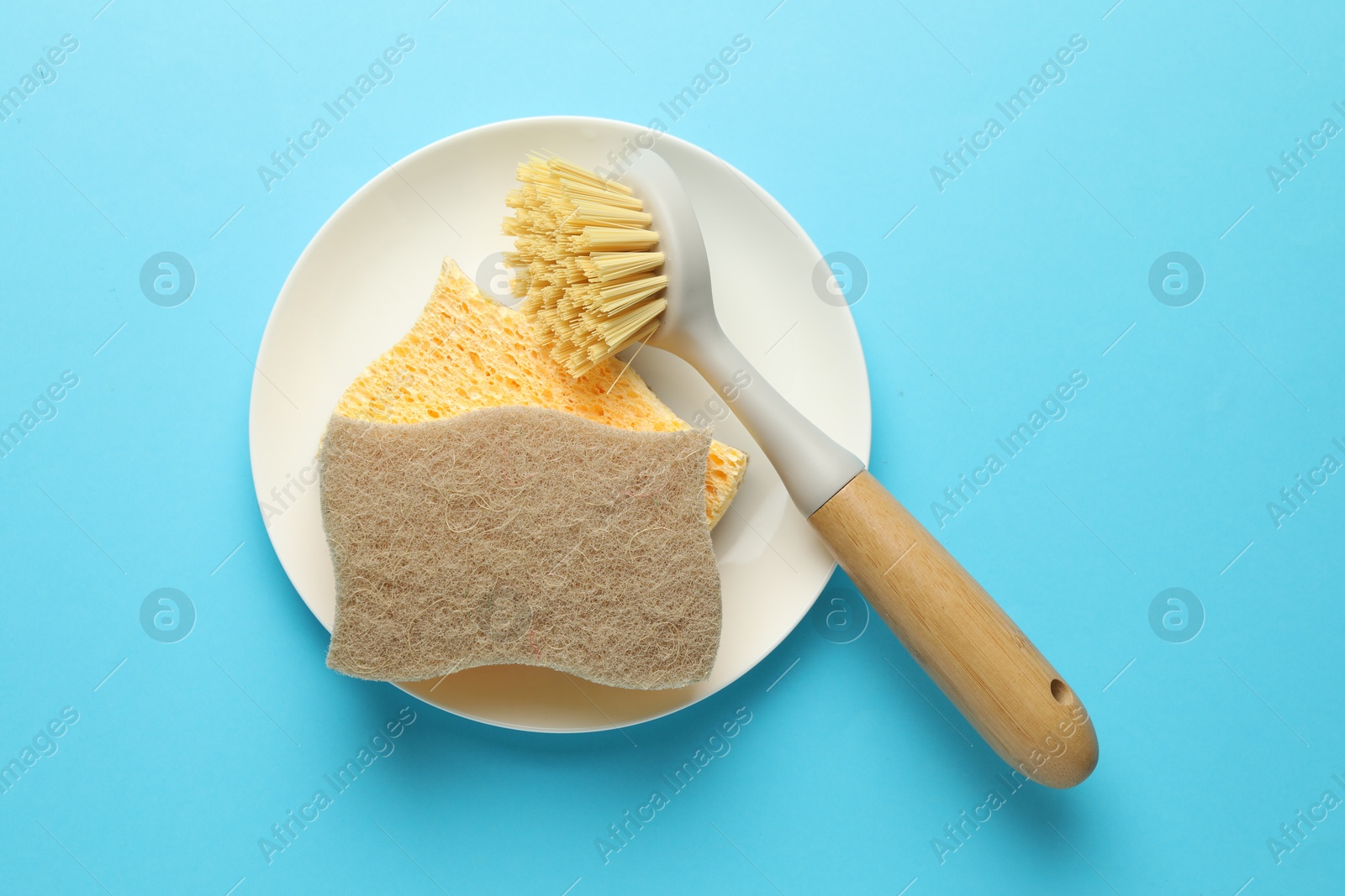 Photo of Sponges, plate and brush on light blue background, top view