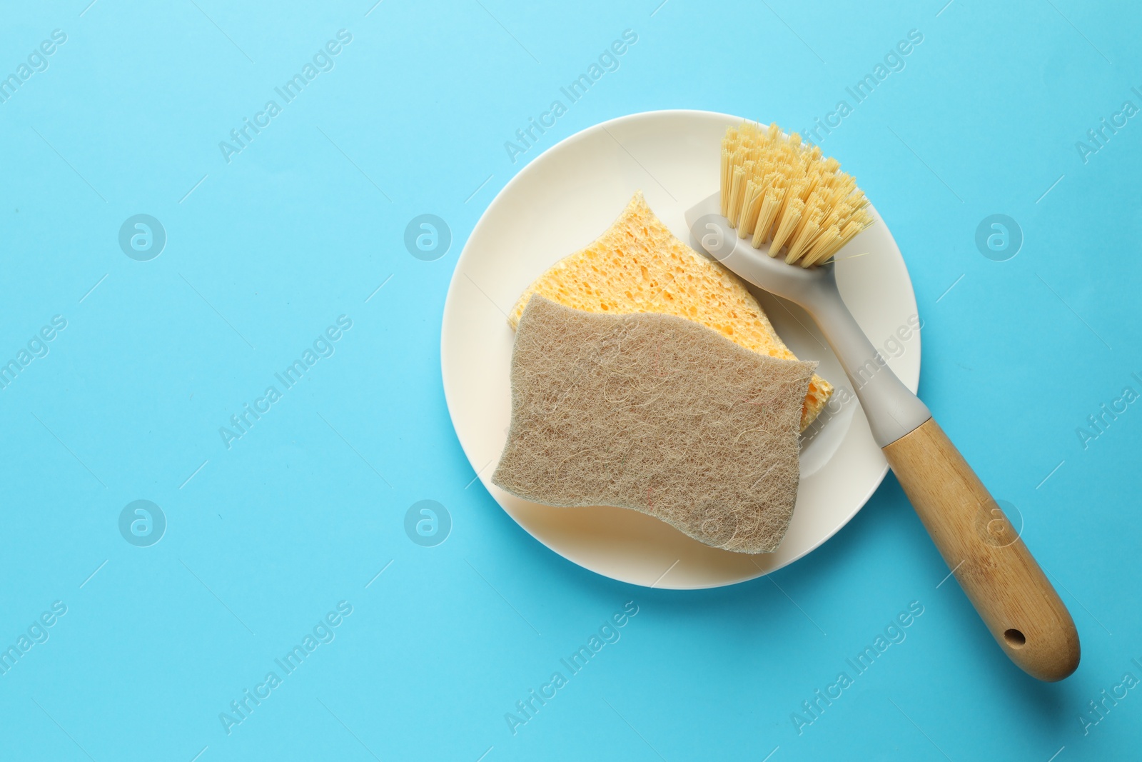 Photo of Sponges, plate and brush on light blue background, top view. Space for text