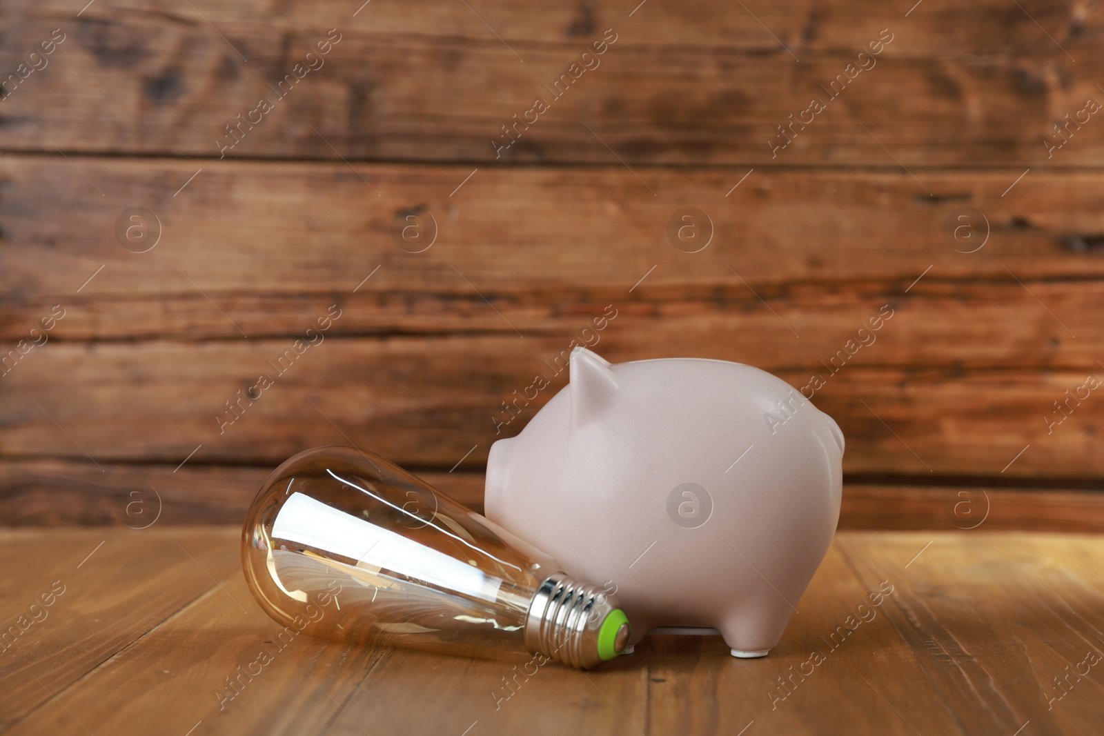 Photo of Piggy bank and light bulb on wooden table. Energy saving concept