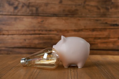 Photo of Piggy bank and light bulb on wooden table. Energy saving concept