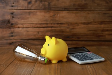 Photo of Piggy bank, calculator and light bulb on wooden table. Energy saving concept