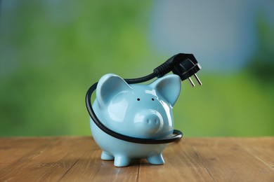 Photo of Piggy bank and plug on wooden table outdoors. Energy saving concept