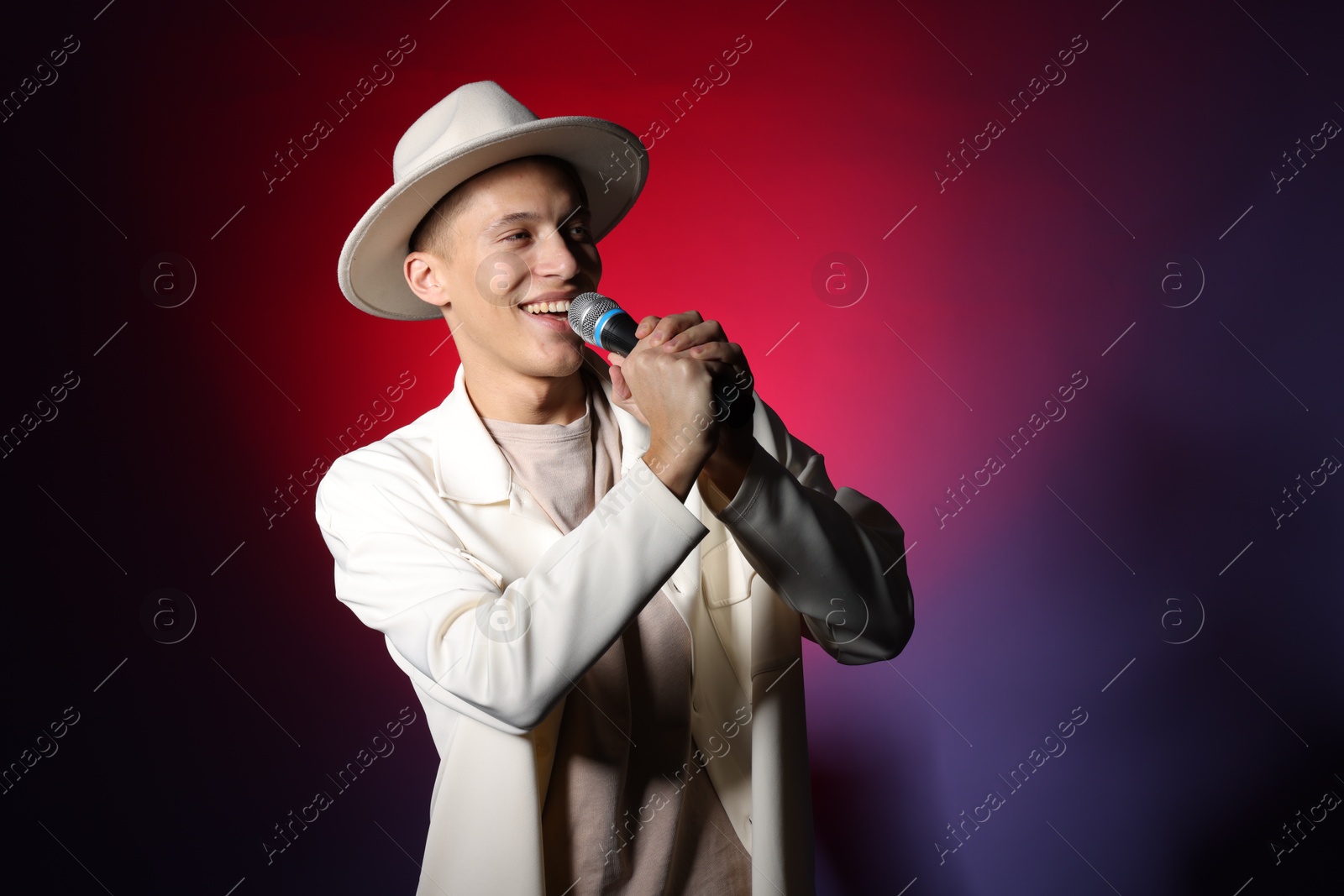 Photo of Talented young man singing on dark background with red light. Space for text