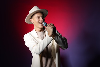 Photo of Talented young man singing on dark background with red light. Space for text