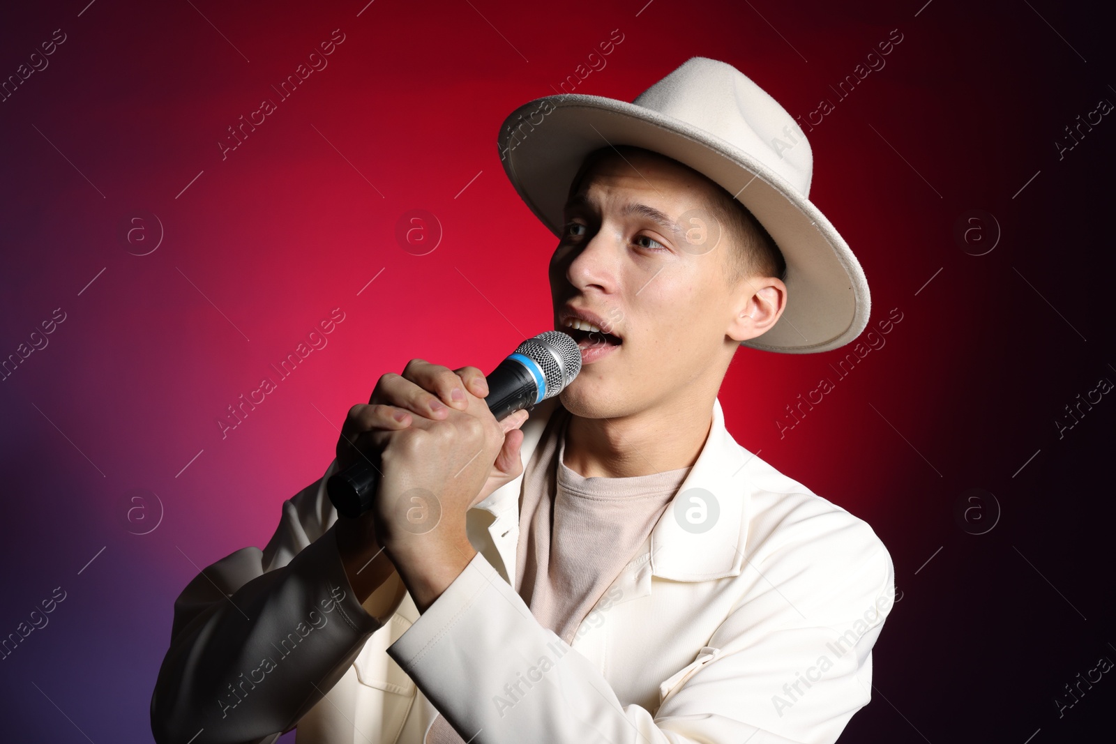 Photo of Talented young man singing on dark background with red light