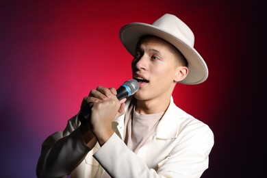 Photo of Talented young man singing on dark background with red light