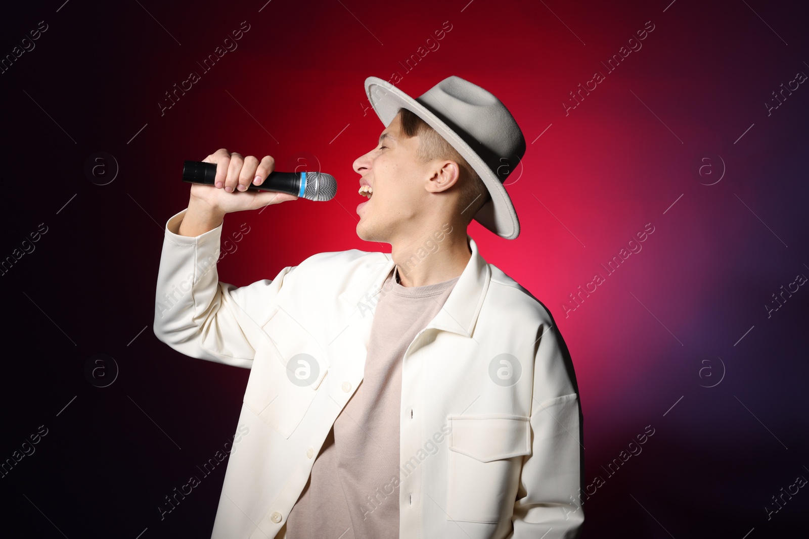 Photo of Talented young man singing on dark background with red light