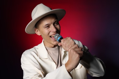 Photo of Talented young man singing on dark background with red light