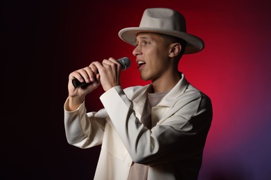 Photo of Talented young man singing on dark background with red light