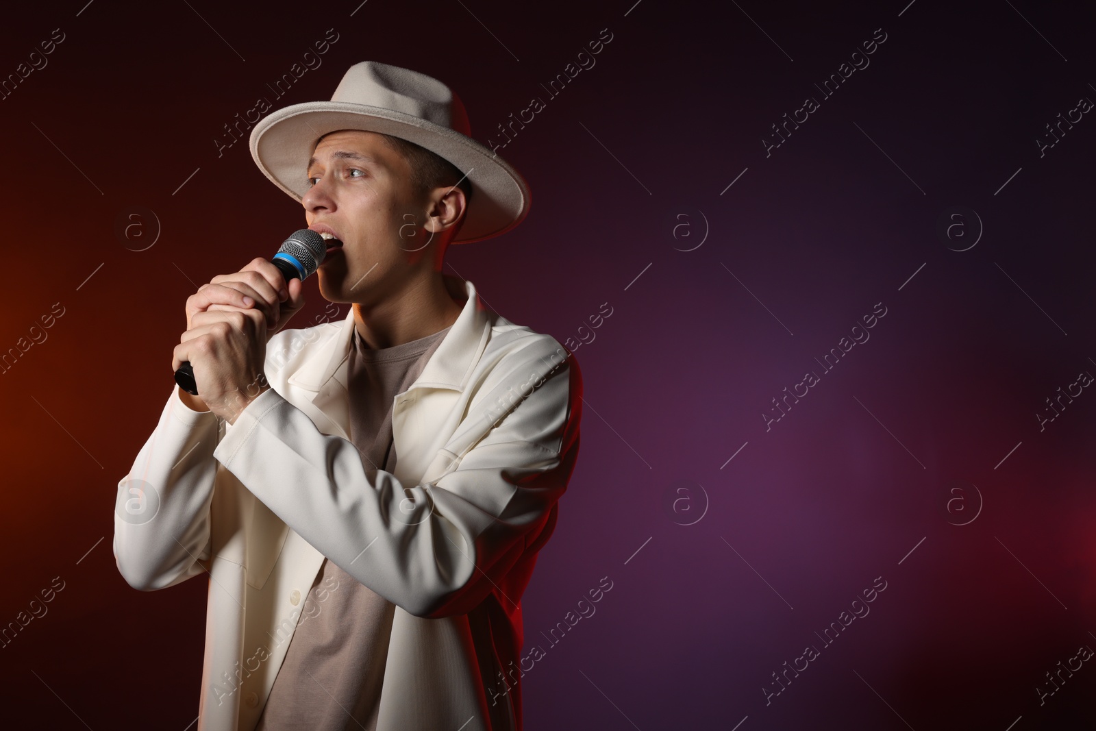 Photo of Talented singer performing on dark background with color lights. Space for text