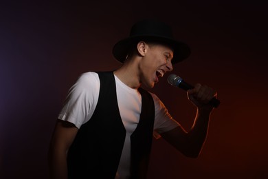 Photo of Talented young man singing on dark background with color light