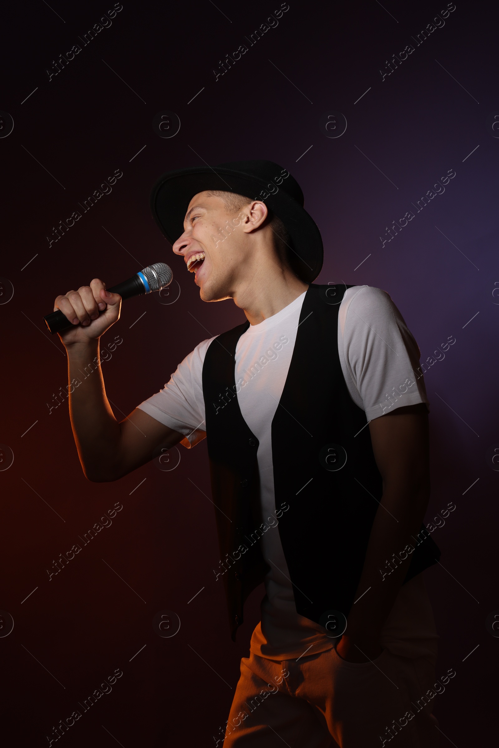 Photo of Talented young man singing on dark background with color light