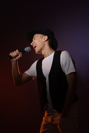 Talented young man singing on dark background with color light