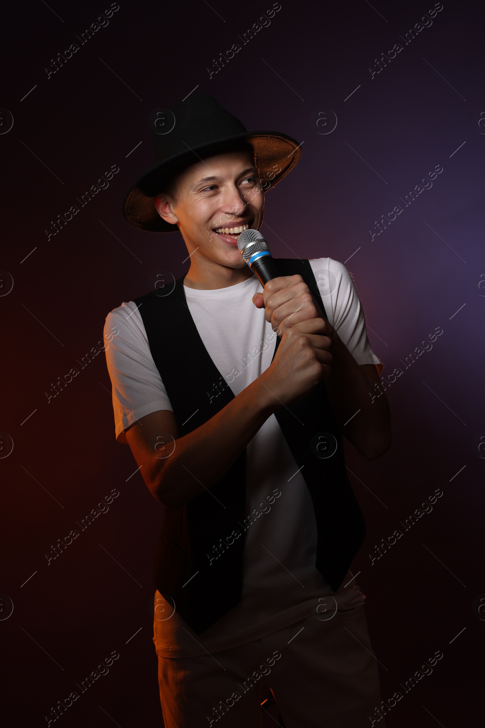 Photo of Talented young man singing on dark background with color light