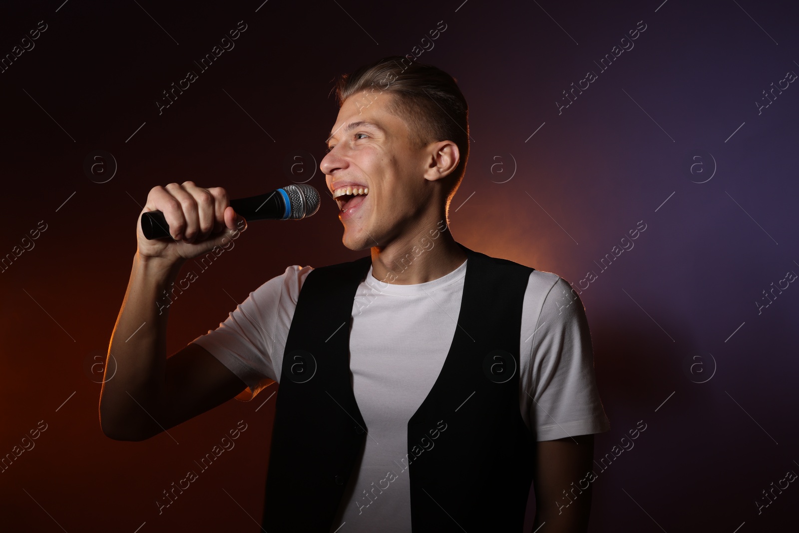 Photo of Talented young man singing on dark background with color light