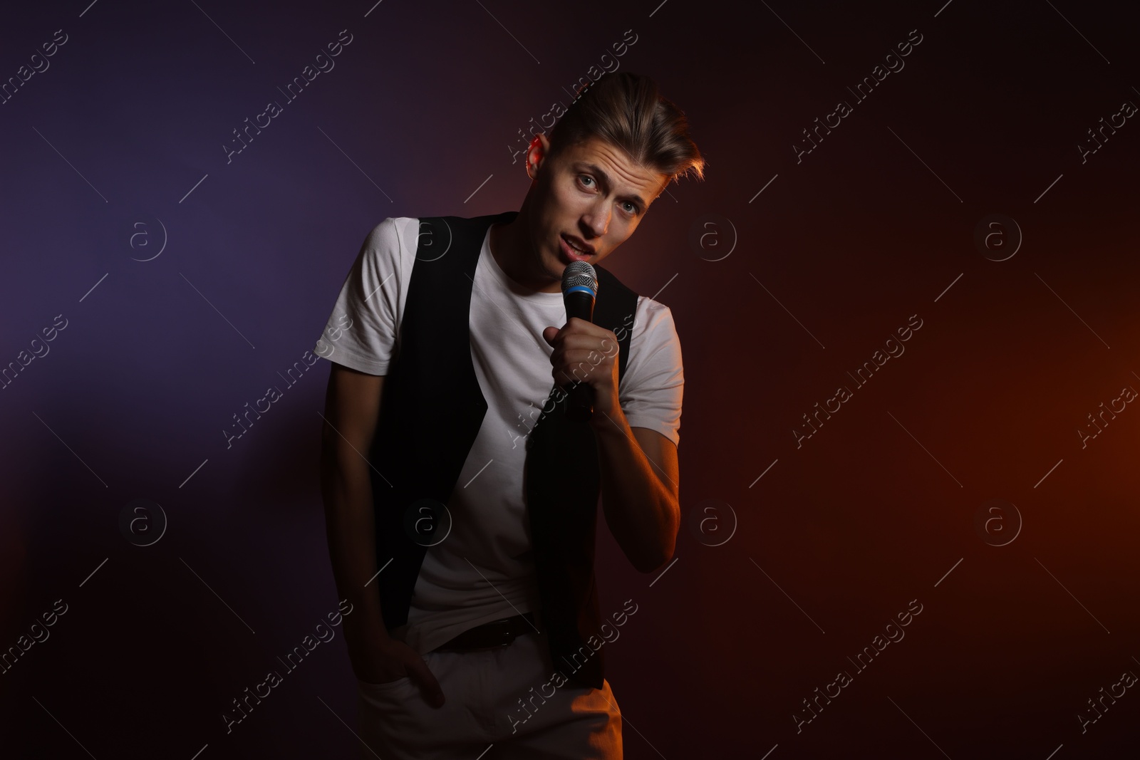 Photo of Talented young man singing on dark background with color light