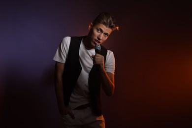 Photo of Talented young man singing on dark background with color light