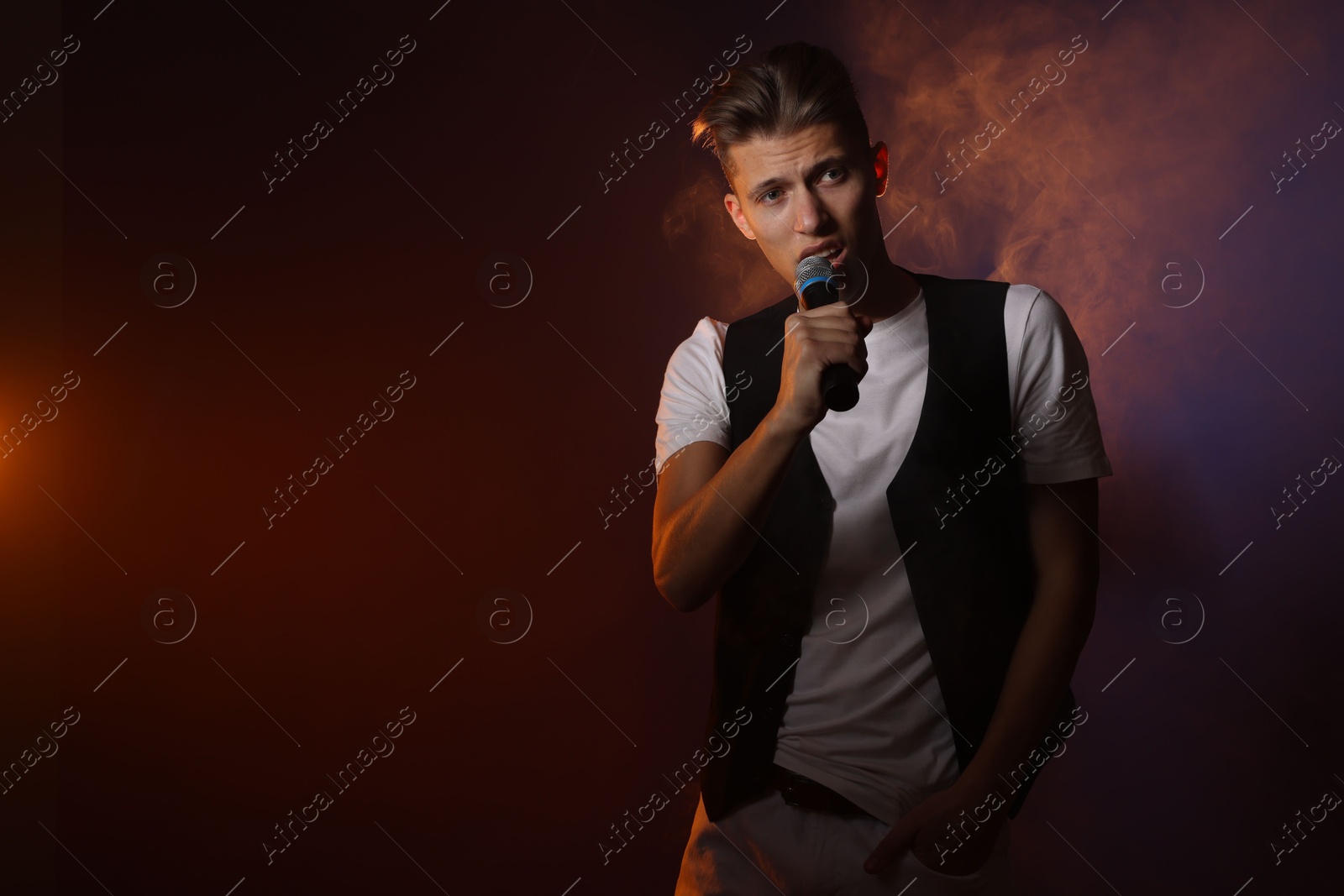 Photo of Talented young man singing on dark background with color light and smoke. Space for text