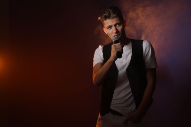 Photo of Talented young man singing on dark background with color light and smoke. Space for text