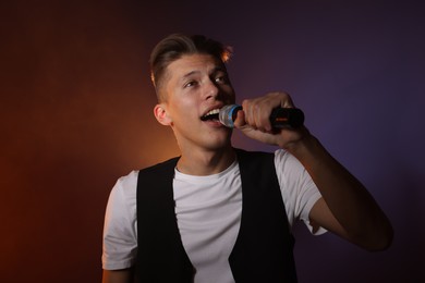 Talented young man singing on dark background with color light and smoke